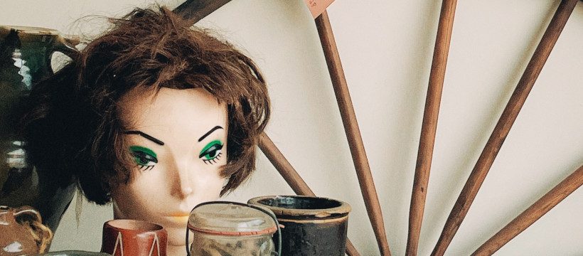 Vente de garage. Des pots et une tête de mannequin sur une table, une roue en bois en arrière-plan.
