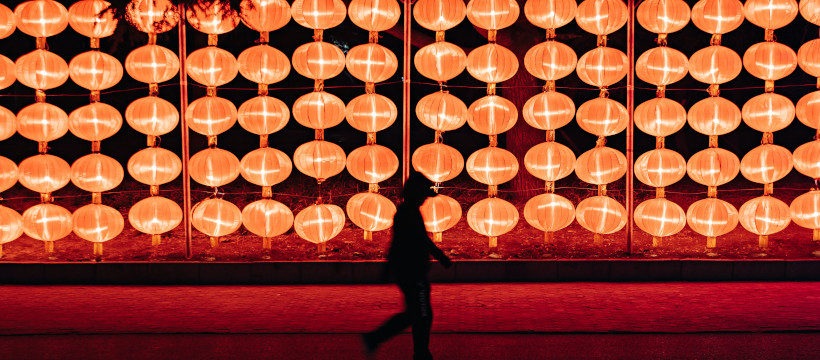 Mur de lanternes en papier rouge, allumées dans la nuit. Une silhouette en contre-jour passe devant.