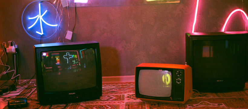Écrans de télévisions cathodiques posés sur un tapis, ambiance de néons rouges.