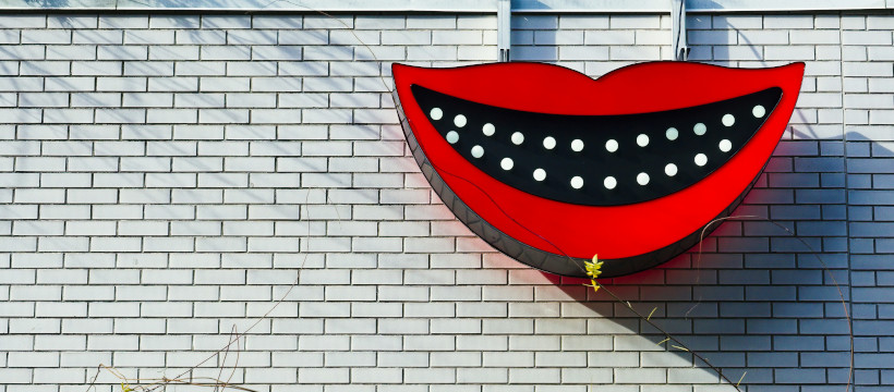Enseigne en forme de bouche souriante sur un mur de briques blanches.