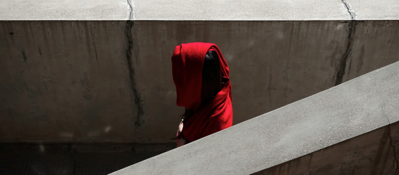 Profil encapuchonné de rouge dans un escalier gris.