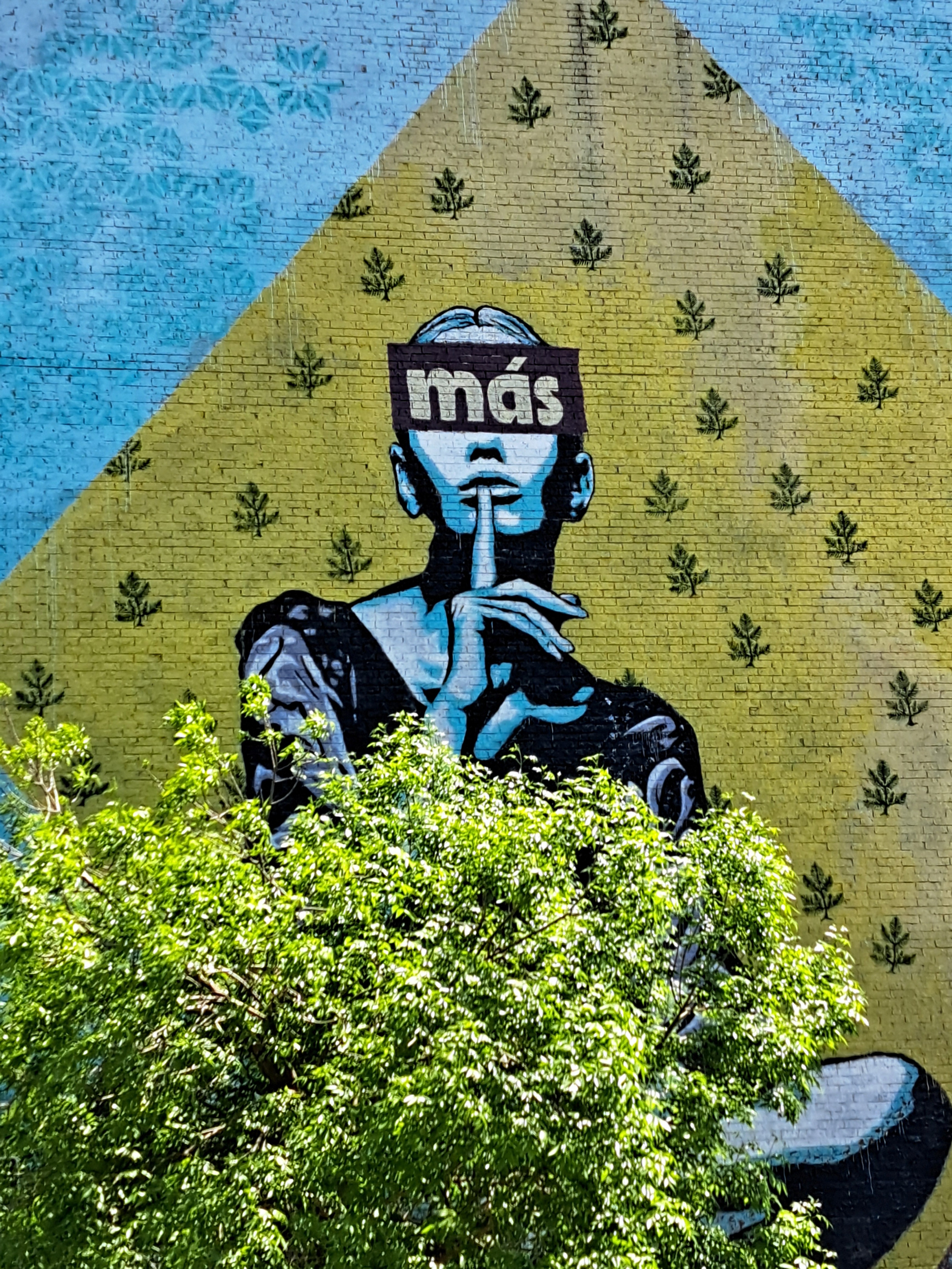murale qui représente une femme faisant le signe de se taire, avec l'inscription « más » sur les yeux