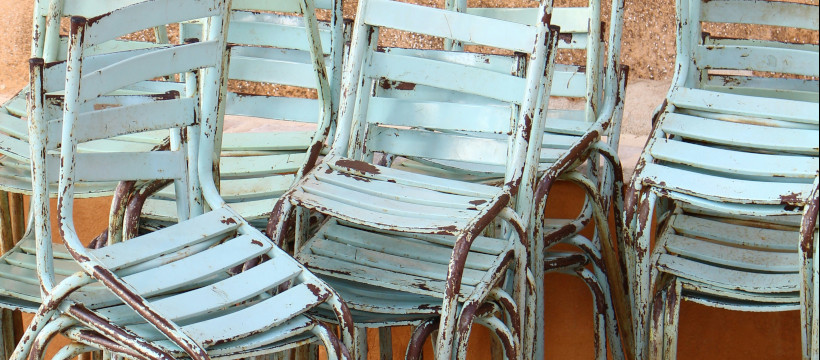 Chaises écaillées empilées devant un mur en crépi.